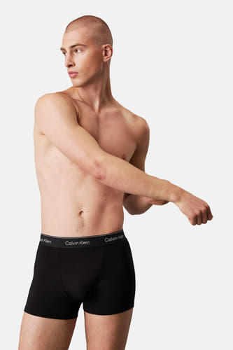 Zwarte boxershort van Calvin Klein, gedragen door een mannelijk model dat zijn rechterarm over zijn borst rekt.