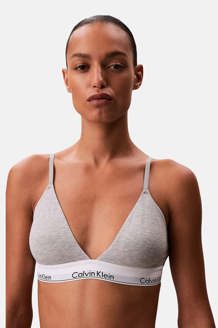 Manteau gris Calvin Klein, avec une bande blanche à logo, porté par un modèle contre un fond blanc.