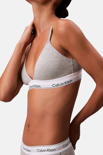 Grijze beha van Calvin Klein, met een witte band met logo, gedragen door een model tegen een witte achtergrond.
