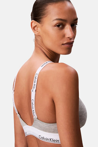 Grijze beha van Calvin Klein, met witte bandjes met logo, gezien van achteren over de schouder.
