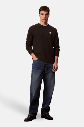 T-shirt noir à manches longues de Calvin Klein, porté avec des jeans larges et des chaussures noires.