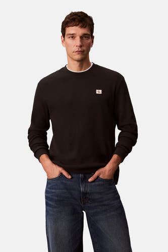 T-shirt noir à manches longues de Calvin Klein, avec un logo subtil sur la poitrine et porté avec des jeans bleus.