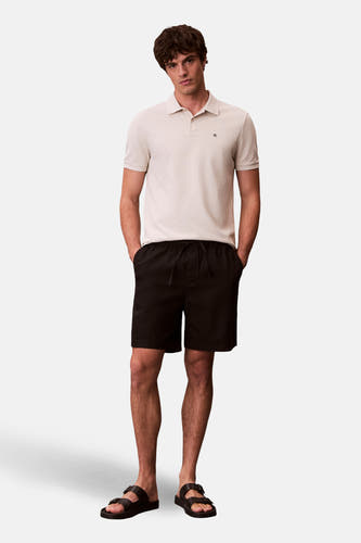 Ecru polo met korte mouwen van Calvin Klein, gedragen met zwarte shorts en sandalen.