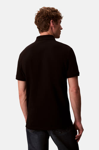 Zwarte polo met korte mouwen van Calvin Klein, achterkant gezien, gecombineerd met een donkere jeans.
