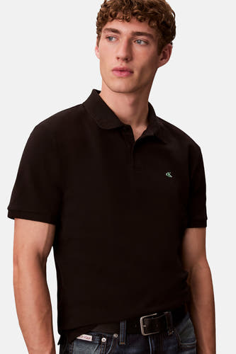Zwarte polo met korte mouwen van Calvin Klein, met een klein logo en gedragen met een zwarte riem en jeans.
