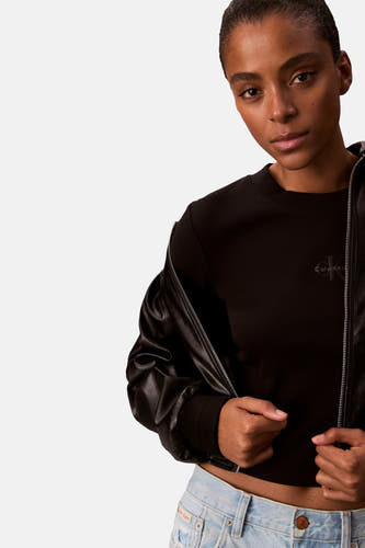 T-shirt noir à manches longues de Calvin Klein, avec un logo subtil et porté avec une veste en cuir et des jeans.