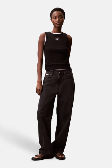 Zwarte singlet van Calvin Klein met een wit logo op de borst en gedragen met wijde, donkere jeans.
