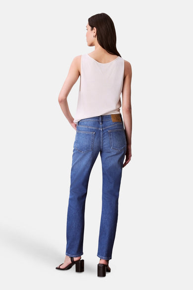 Jean slim de denim bleu Calvin Klein, vu de de derrière, associé à une chemise sans manches et des baskets noires.