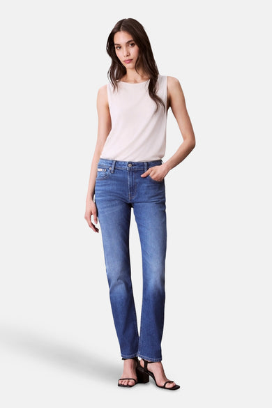 Jean slim en bleu moyen denim de Calvin Klein, associé à une chemise blanche et des baskets noires.