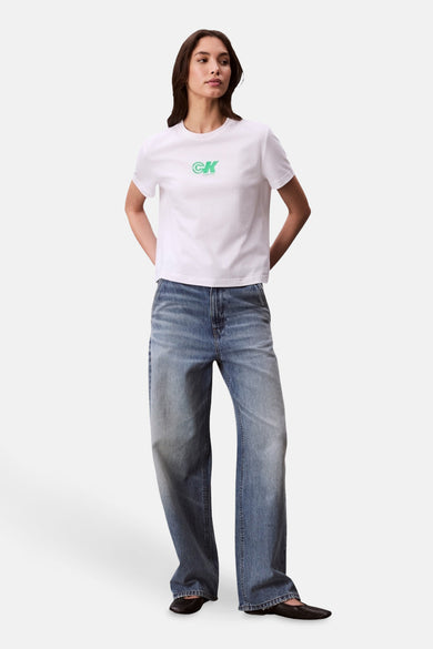 T-shirt blanc à manches courtes de Calvin Klein, porté avec des jeans larges et des chaussures plates.