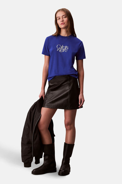 Blauw T-shirt met korte mouwen van Calvin Klein, gedragen met een zwarte leren rok en laarzen, met een zwarte jas in de hand.