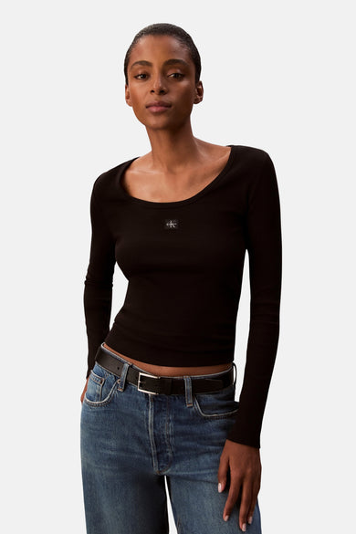T-shirt noir à manches longues de Calvin Klein, texture côtelée, porté avec un jean bleu et une ceinture noire.