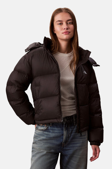 Zwarte korte jas van Calvin Klein, met een donsgevulde textuur en een logo op de borst, gedragen met een beige trui en jeans.
