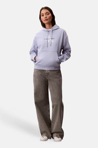 Pull-over marron avec capuche de Calvin Klein, porté avec des jeans gris et des chaussures blanches.