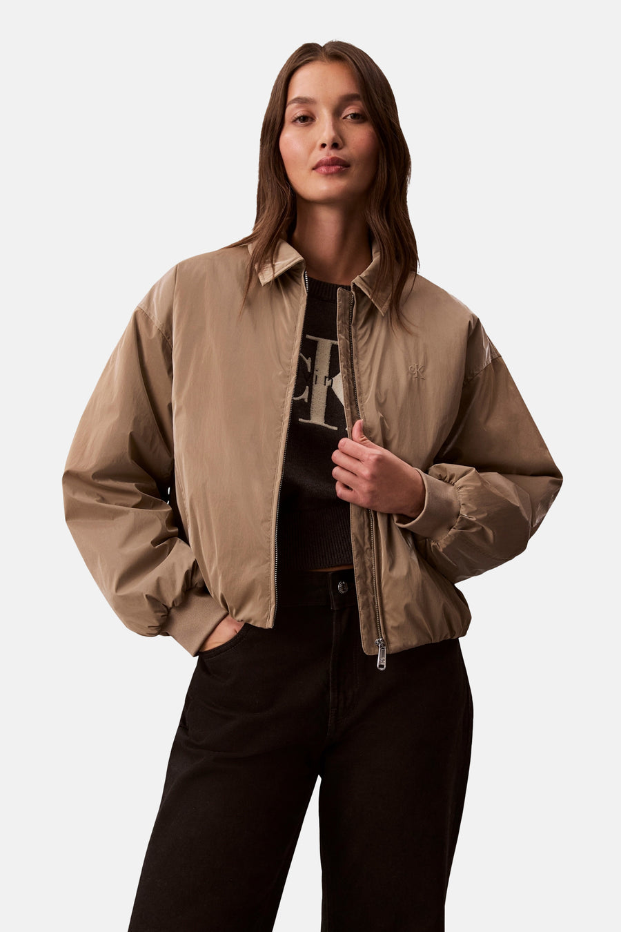 Beige korte jas van Calvin Klein, met zichtbare ritssluiting en gedragen over een donkere trui en broek.