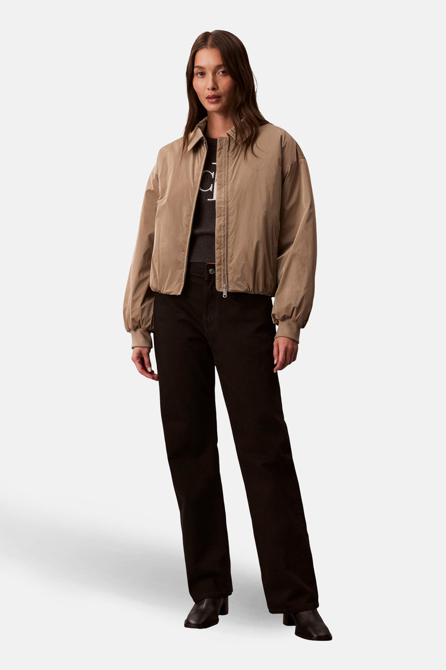 Beige korte jas van Calvin Klein, met lange mouwen, gedragen met een donkere trui en zwarte broek.
