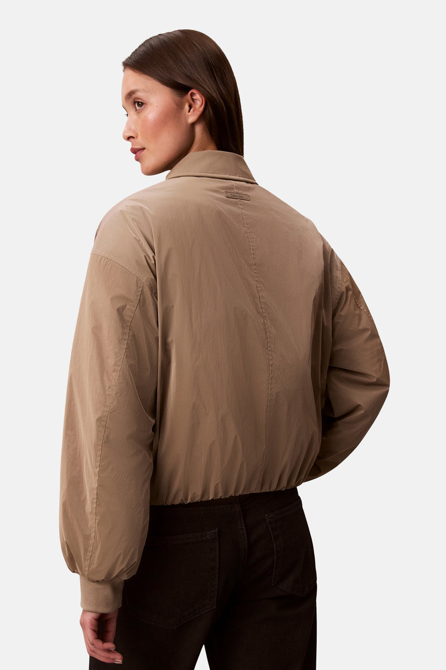 Beige korte jas van Calvin Klein, met lange mouwen en een donkere broek.
