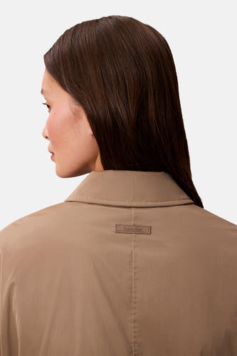 Beige korte jas van Calvin Klein, met merkembleem op de rug.
