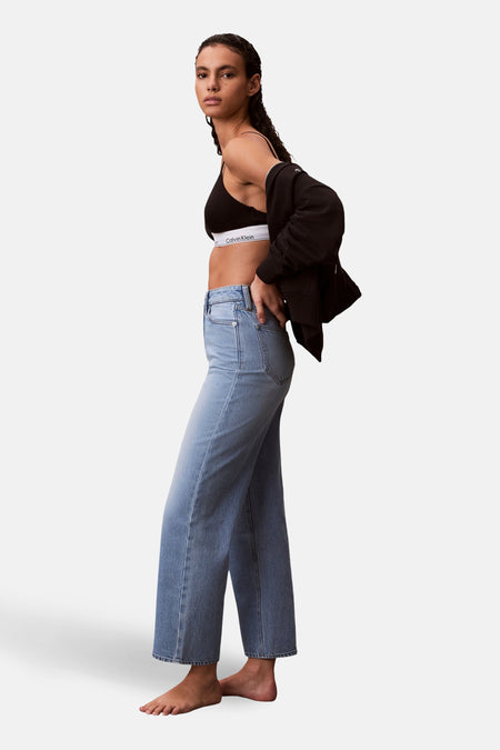 Jeans special fit van lichtblauw denim van Calvin Klein, met een model in een zwarte top en jas, staand.
