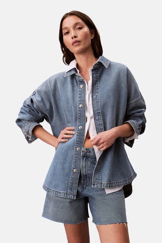 T-shirt en jeans en denim bleu moyen de Calvin Klein, porté sur un chemisier blanc à col boutonné.
