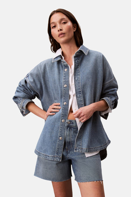 T-shirt en jeans en denim bleu moyen de Calvin Klein, porté sur un chemisier blanc à col boutonné.