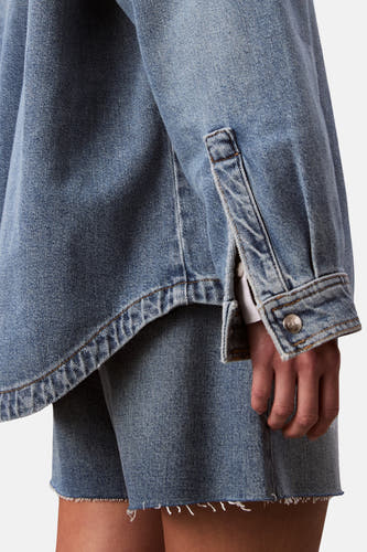T-shirt en jeans en denim bleu moyen de Calvin Klein, avec des manches longues et une fermeture à boutons, dans un cropped shot.