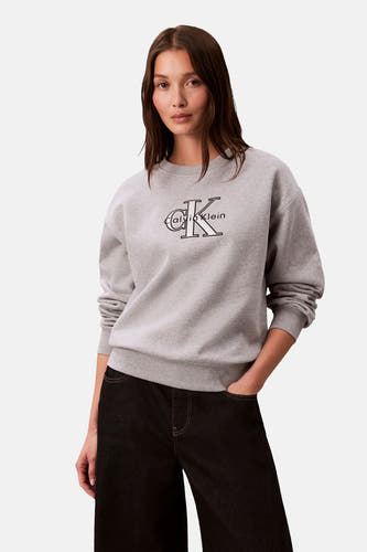 Grijze sweater met ronde hals van Calvin Klein, met logo op de voorkant, gecombineerd met een donkere broek.
