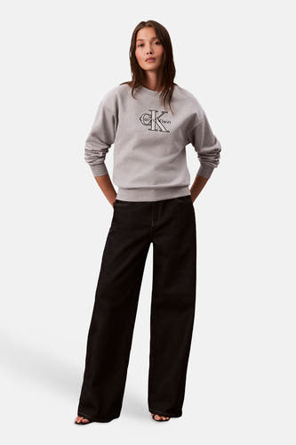 Grijze sweater van Calvin Klein, met het logo gedrukt op de voorkant, gedragen met een donkere jeans.
