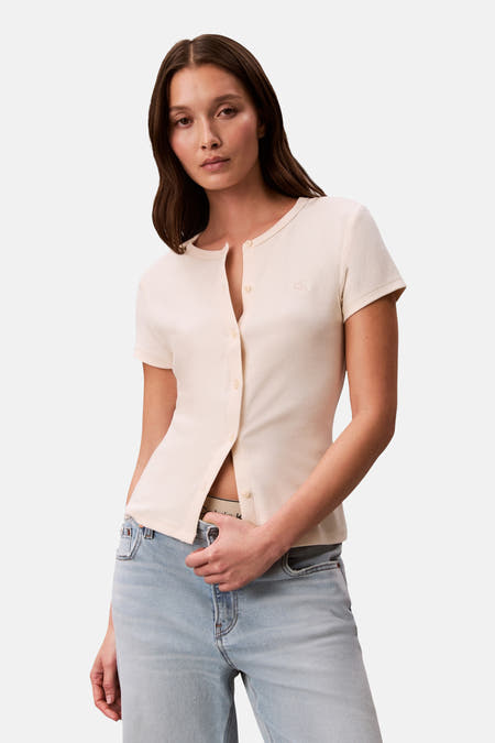 Ecrukleurig gilet van Calvin Klein, met korte mouwen en knoopsluiting, gedragen met een blauwe jeans.
