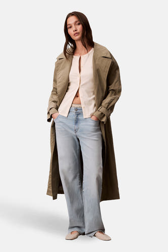 Ecru gilet van Calvin Klein, gedragen met een beige vest en wijde jeans met een lange trenchcoat.
