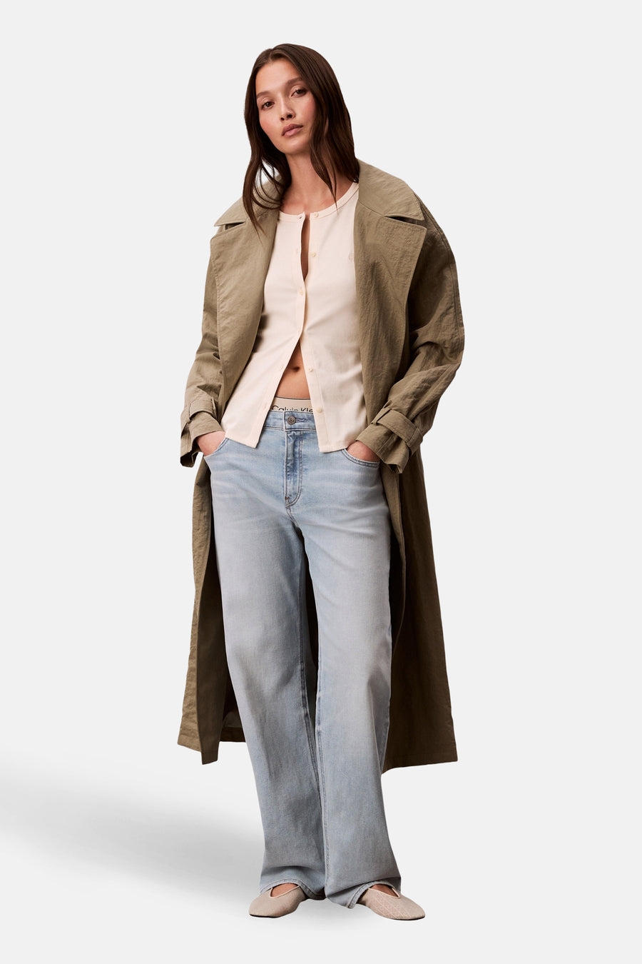 Ecru gilet van Calvin Klein, gedragen met een beige vest en wijde jeans met een lange trenchcoat.
