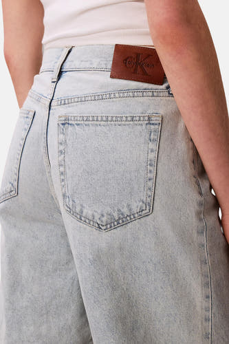Short en jean bleu clair de Calvin Klein, avec écusson logo marron sur la ceinture.