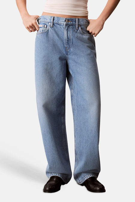 Jean en denim bleu clair Calvin Klein, à jambes larges et coupe décontractée, porté avec un crop top beige et des mocassins noirs.