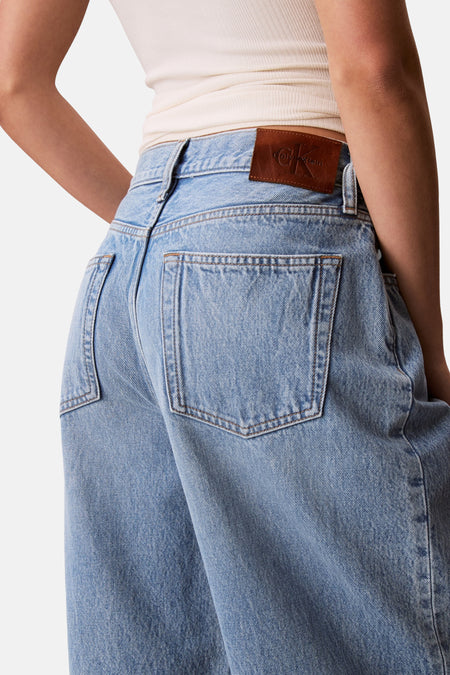 Jean en denim bleu clair Calvin Klein avec écusson logo en cuir marron, poches arrière et un haut légèrement côtelé.