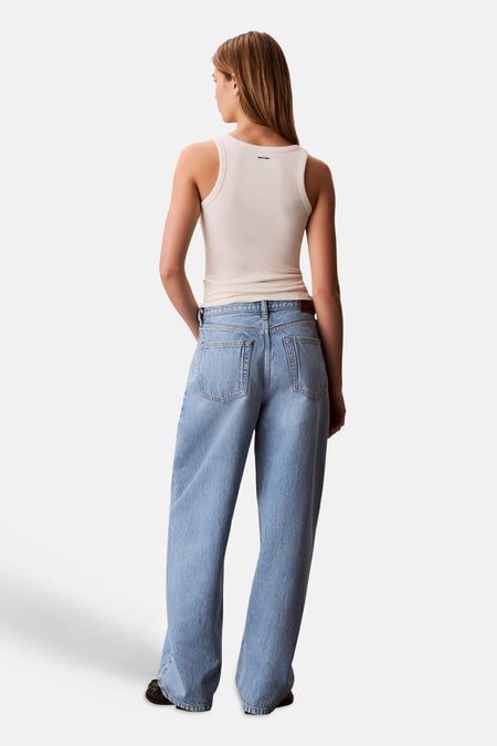 Jean en denim bleu clair coupe spéciale Calvin Klein, coupe ample avec poches arrière, porté avec un débardeur beige et des chaussures noires, vu de dos.
