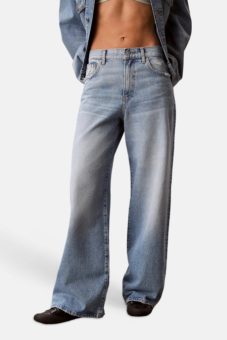 Jean large bleu clair en denim de Calvin Klein, porté par un mannequin et associé à une veste en jean assortie, vu de dos.