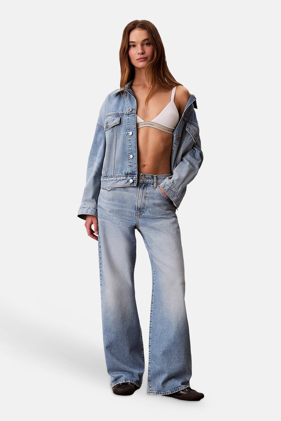 Lichtblauwe wide-leg jeans van denim van Calvin Klein, gedragen door een model met een spijkerjasje en witte bralette.