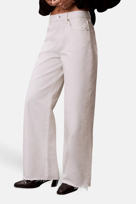 Wijde jeans van off-white denim van Calvin Klein, met rafelige zomen en metalen details, gedragen met donkere schoenen.