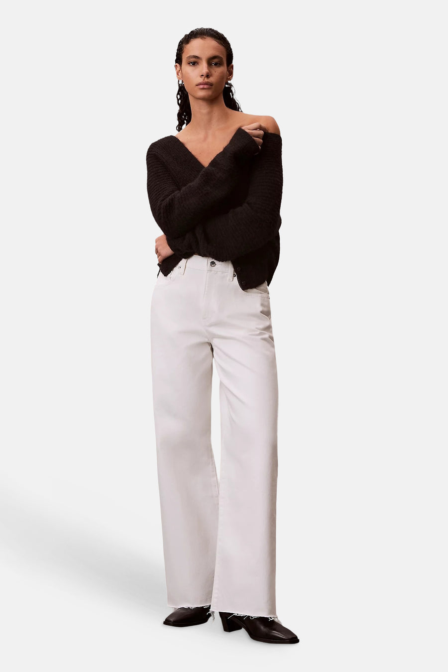 Gebroken witte wide-leg jeans van denim van Calvin Klein met gerafelde zomen, gedragen door een model met een zwarte trui en enkellaarsjes.