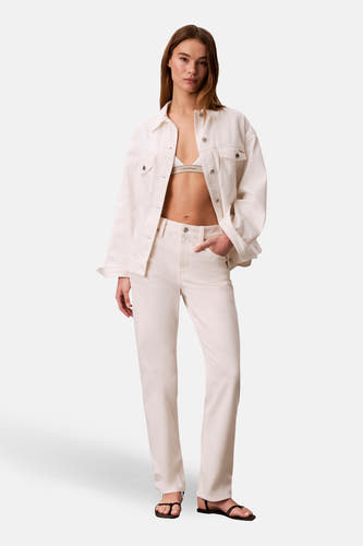 Veste courte en jean blanc cassé de Calvin Klein, portée avec un soutien-gorge Calvin Klein et un jean blanc cassé avec des sandales.