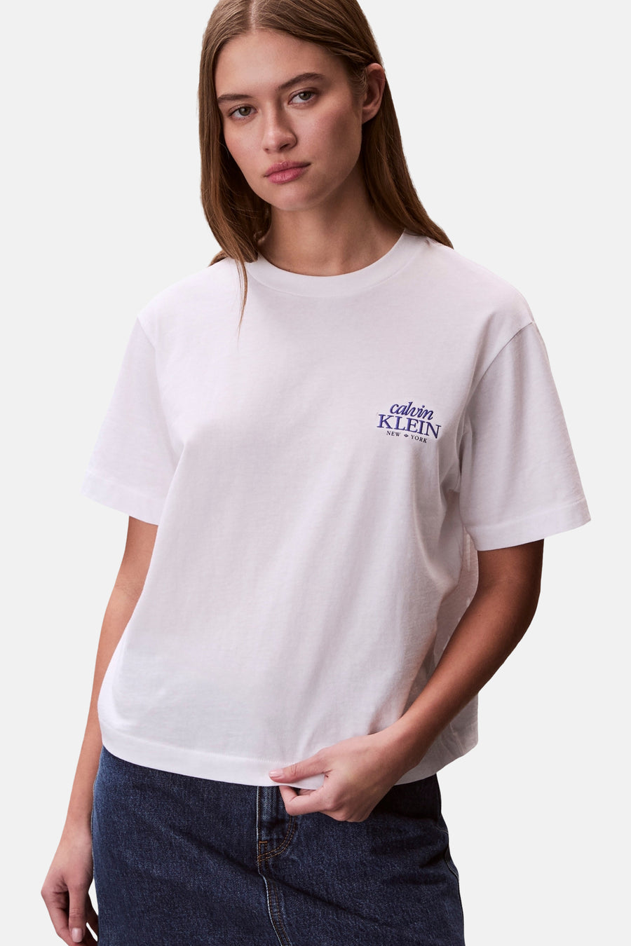 T-shirt blanc à manches courtes Calvin Klein, avec logo sur la poitrine, associé à un jean foncé.