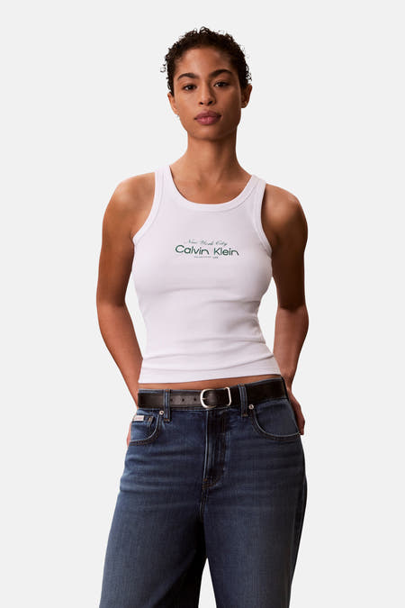 Débardeur blanc Calvin Klein, avec impression de logo, combiné avec un jean bleu foncé et une ceinture en cuir noir.