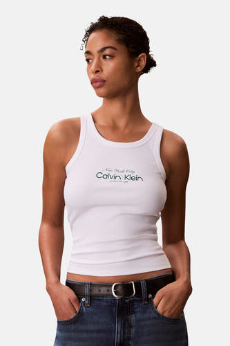 Witte tanktop van Calvin Klein, met geribbelde textuur en een donkergroen logo op de borst, gedragen met een jeans en riem.
