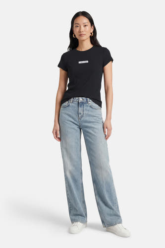 T-shirt noir à manches courtes de Calvin Klein, porté avec un jean bleu et des baskets blanches.