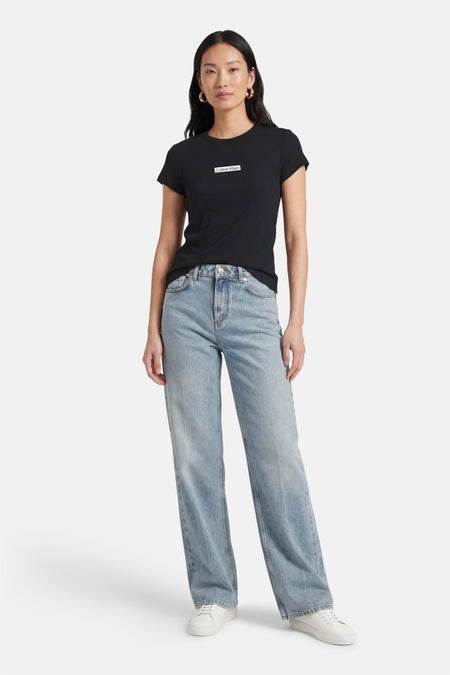 T-shirt noir à manches courtes de Calvin Klein, porté avec un jean bleu et des baskets blanches.