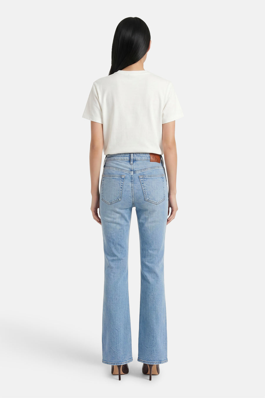 Lichtblauwe skinny bootcut jeans van Calvin Klein, achterzijde met bruin label, model draagt wit T-shirt en hoge hakken
