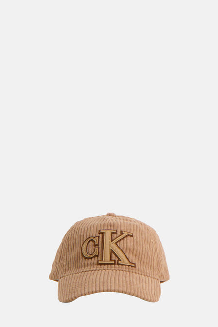 Bruine pet van Calvin Klein, met een 'CK'-logo van corduroy aan de voorkant.

