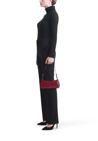 Vrouw met zwarte coltrui en broek, rode handtas, zwarte pumps, staand.
