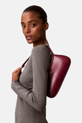 Rode schoudertas van Calvin Klein, gedragen door een model in een grijze jurk, zijaanzicht.