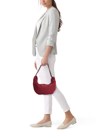Bordeaux schoudertas van Calvin Klein, gedragen door een vrouw met een grijze blazer, witte broek en beige loafers.
